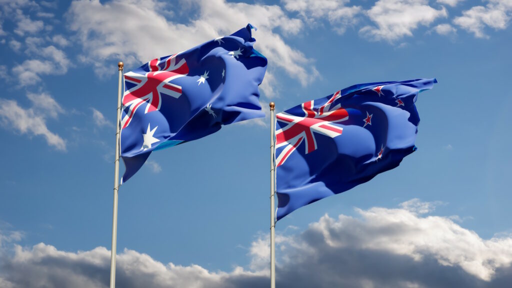Flags of Australia & New-Zealand waving beneath a partly cloudy blue sky
