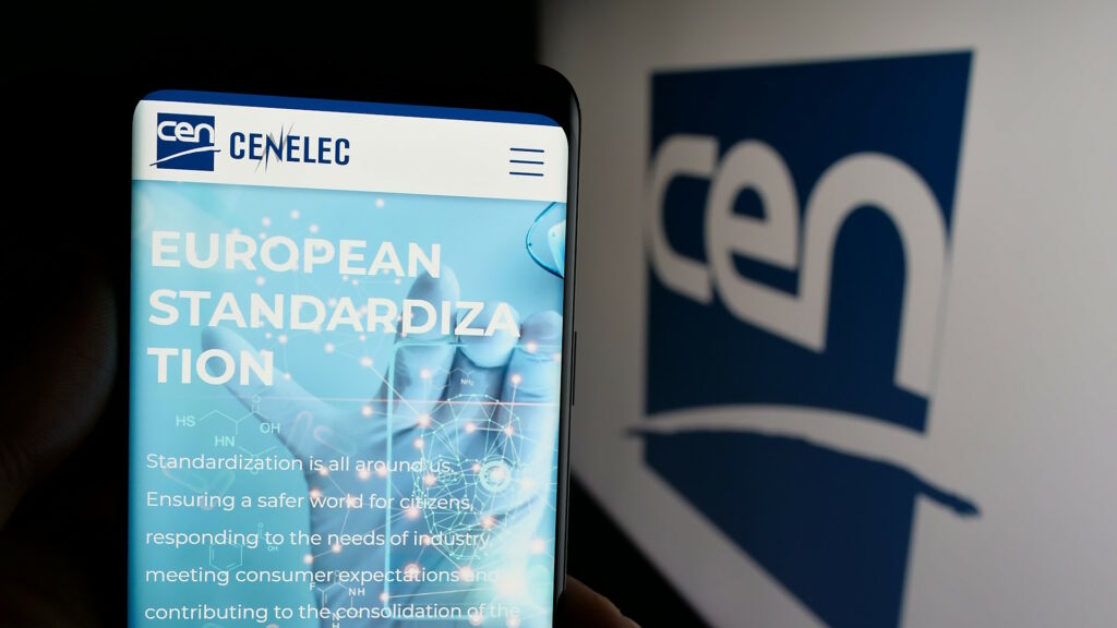 Article on CENELEC displayed on a smartphone screen, in front of a desktop screen showing a CEN logo