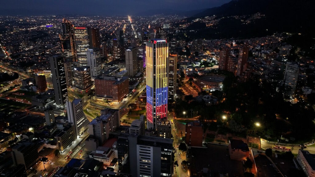 Photo of Bogota by night, showing a skyscraper with Colombia's flag colors