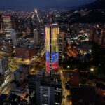 Photo of Bogota by night, showing a skyscraper with Colombia's flag colors