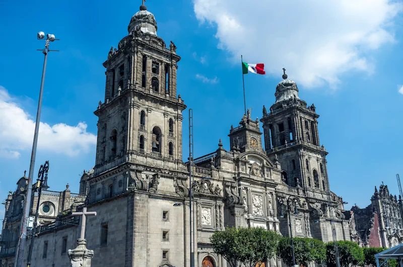 Facade of Mexico City's cathedral, with a Mexican flag waving