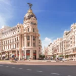 Iconic street view of Calle Alcalá and Gran Vía, showing a busy urban avenue with historic and modern buildings, traffic, and pedestrians on a clear day, in Madrid, capital of Spain