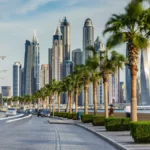 Seaside promenade on Palm Jumeirah, with palm-lined roads and light traffic before sunset, and the Dubai Marina towers visible in the background, in Dubai, United Arab Emirates.