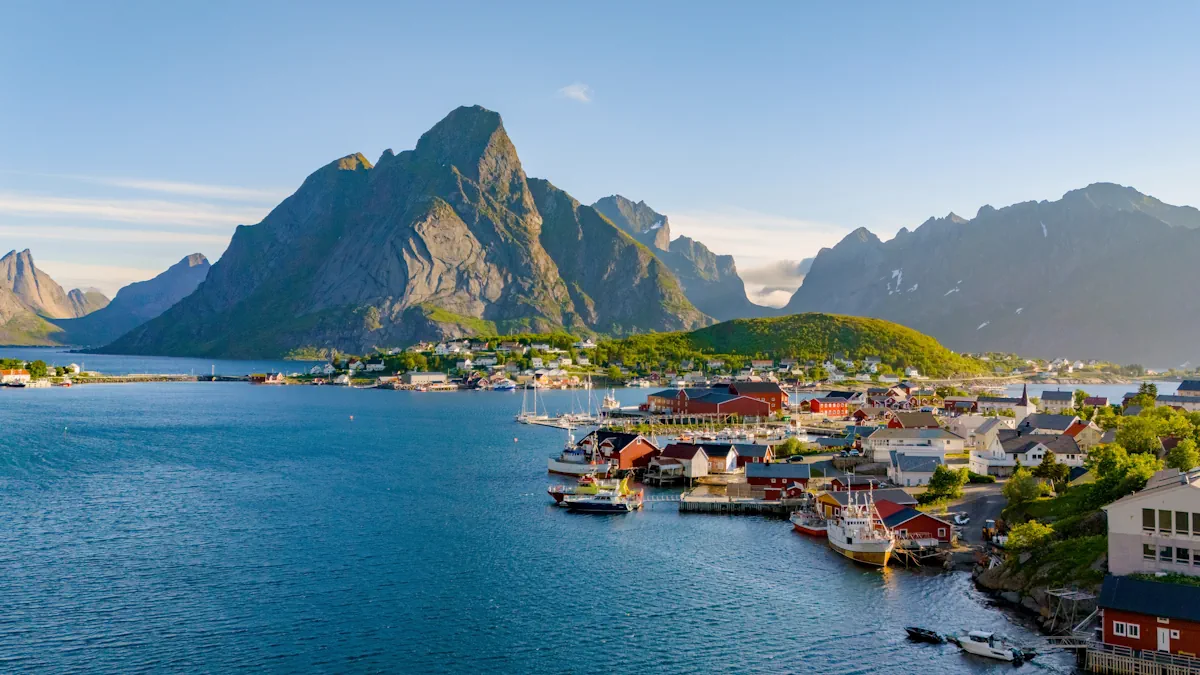 Scenic view of Reine village in the Lofoten Islands, showing traditional red and white houses along the shoreline surrounded by steep mountains and clear blue water.