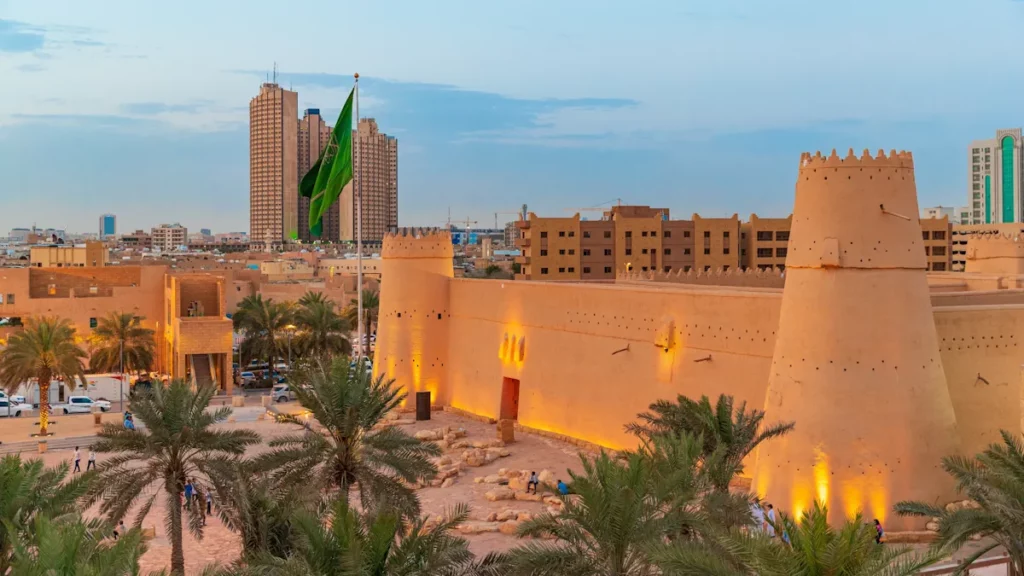 Sunset view of Masmak Palace in central Riyadh, Saudi Arabia, featuring the historic fortress illuminated by warm light and surrounded by Saudi flags.