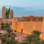 Sunset view of Masmak Palace in central Riyadh, Saudi Arabia, featuring the historic fortress illuminated by warm light and surrounded by Saudi flags.