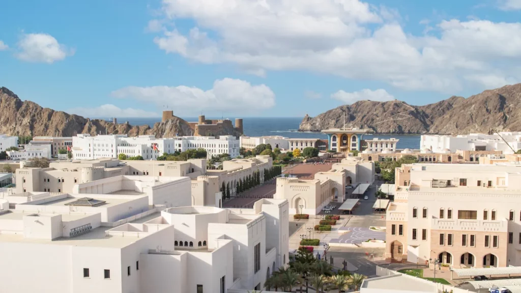 Muscat, Oman, with white buildings spread across the capital city and surrounded by rugged mountains and dramatic rocky landscapes.