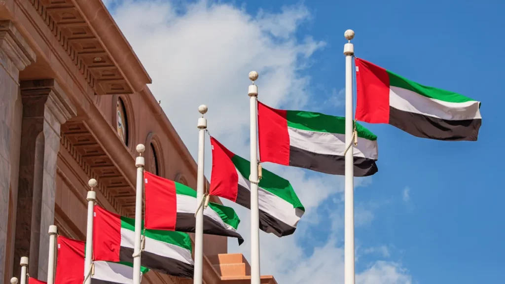 Multiple UAE flags flying on tall poles under a clear blue sky in Abu Dhabi.