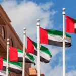 Multiple UAE flags flying on tall poles under a clear blue sky in Abu Dhabi.